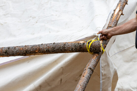 Parents, Quebec, 19 May 2026 : A person's hand secures two wooden logs with yellow rope against a white canvas structure.