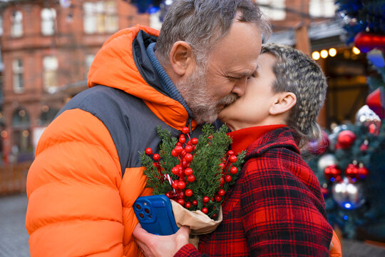 Couple shares a kiss while holding festive decorations in a lively market during the holiday season