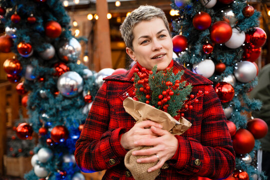 Woman holds flowers at a holiday market surrounded by colorful decorations and lights in winter season