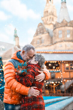 Couple embraces happily in snowy city square in front of historic building during winter celebration