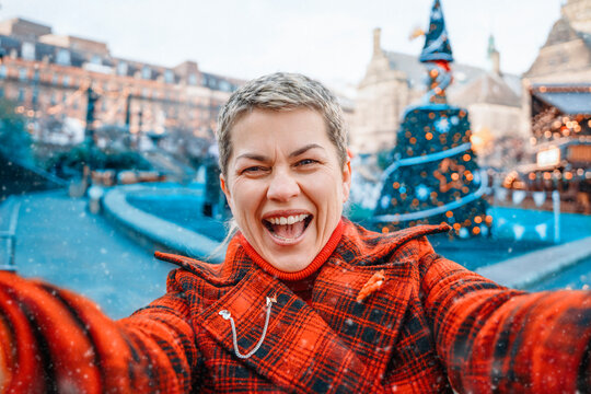 Smiling woman takes selfie in festive square with holiday decorations and events happening during winter season