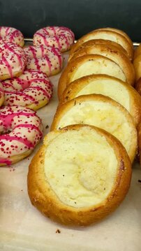 Poppy kolaches and pink glazed donuts in display, cheese and custard fillings, powdered sugar and sprinkles, cafe case presentation, morning treat