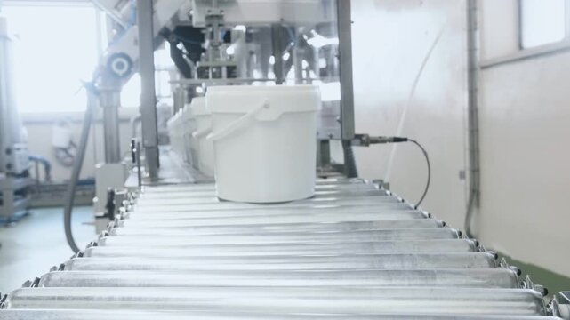 White industrial buckets moving along a conveyor belt inside a modern processing factory, illustrating large-scale automated manufacturing and packaging operations