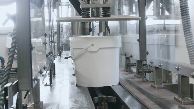 White plastic buckets moving through an advanced automated packaging line inside a bright industrial food processing factory with modern machinery and equipment