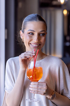 Close up portrait of a smiling young woman drinking an orange cocktail through a straw