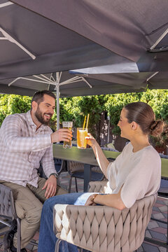 Cheerful couple toasting with beer and cocktail glasses at an outdoor restaurant bar