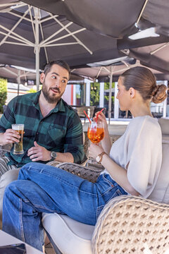 Young couple relaxing in comfortable lounge chairs and talking at an outdoor cafe terrace