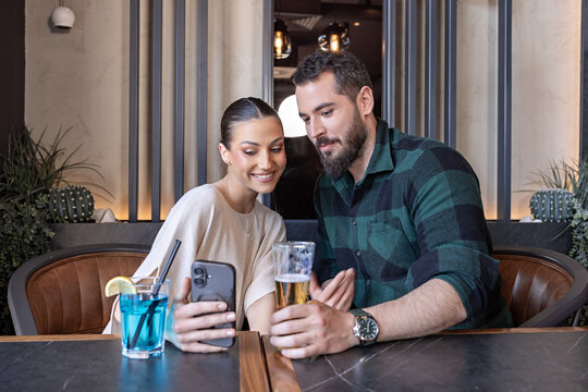 Happy young couple looking at a smartphone screen together in a modern restaurant interior