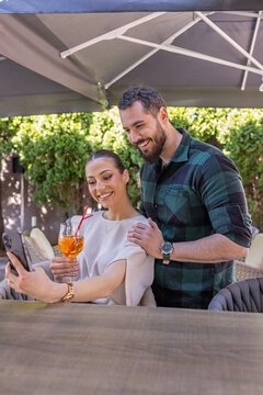 Smiling young couple taking a selfie with a smartphone at an outdoor terrace cafe