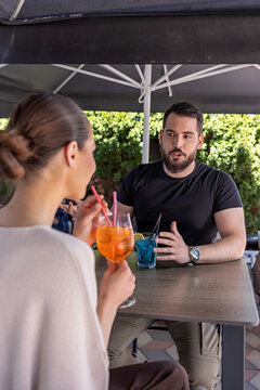 Young couple talking and drinking cocktails at an outdoor cafe terrace