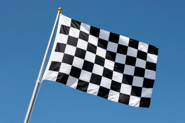 Obraz premium Black and white checkered flag flutters against a clear blue sky. Wind carries the flag with dynamic motion.