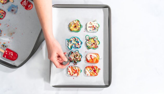 Hand decorating colorful Funfetti cookies with sprinkles on a baking sheet