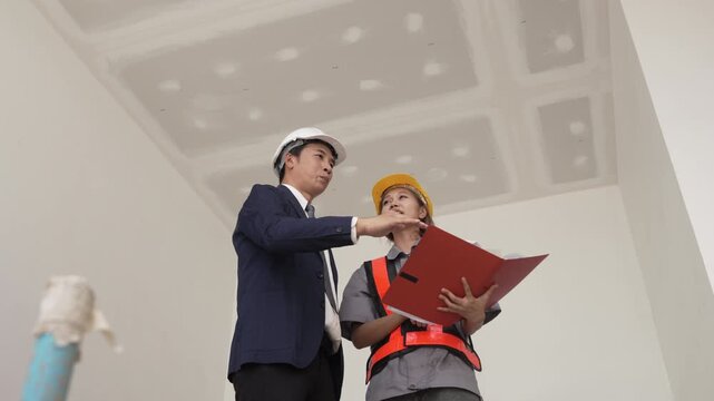 Male and female construction engineers inspecting unfinished room and checking installation details at building site.