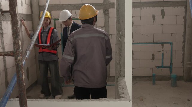 Two construction workers wearing safety helmets discussing renovation progress and reviewing plans inside unfinished building interior.