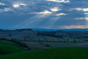 Obraz premium Dramatic sunbeams breaking through clouds over Tuscany rolling hills landscape, Italy