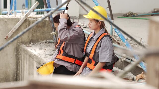 Two construction workers wearing safety helmets discussing renovation progress and reviewing plans inside unfinished building interior.