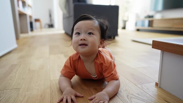 Adorable child smiles, lying on wooden floor. Bright eyes show joy, soft cheeks gleam with happiness. Little hands rest gently on warm wood planks. Child crawls forward, curious gaze fixed on viewer