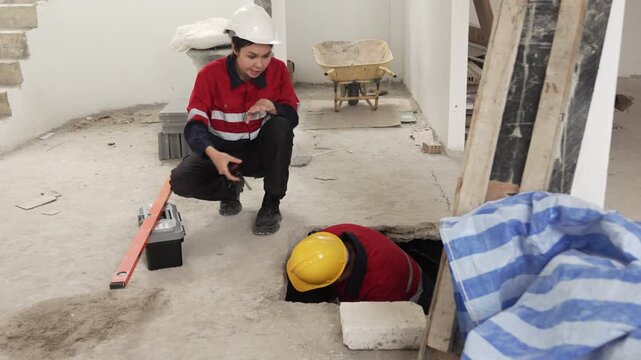 Two construction workers wearing safety helmets discussing renovation progress and reviewing plans inside unfinished building interior.