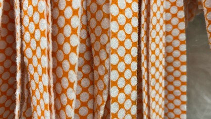 A close-up of the texture of white polka-dot fabric against a bright orange background. The grain details are clearly visible with a natural crease effect. © RiyanBudi