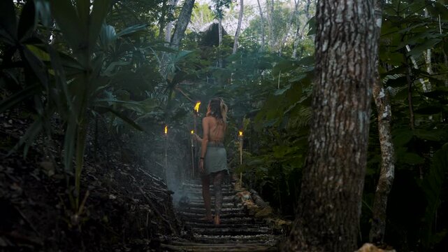 Woman walking through mystical Peten jungle path lit by torches at dusk