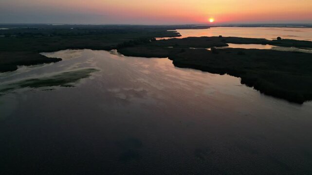 Spectacular high angle view of a golden sunrise over the Danube Delta UNESCO biosphere reserve. Scenic flyover above glowing water channels and wild reed vegetation in Romania.