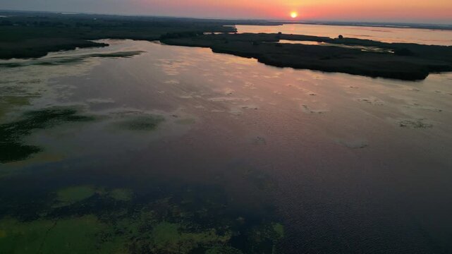Spectacular high angle view of a golden sunrise over the Danube Delta UNESCO biosphere reserve. Scenic flyover above glowing water channels and wild reed vegetation in Romania.