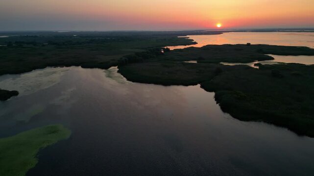 Spectacular high angle view of a golden sunrise over the Danube Delta UNESCO biosphere reserve. Scenic flyover above glowing water channels and wild reed vegetation in Romania.