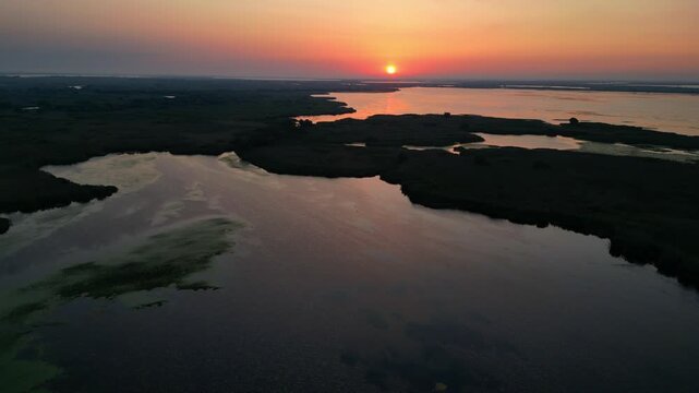 Spectacular high angle view of a golden sunrise over the Danube Delta UNESCO biosphere reserve. Scenic flyover above glowing water channels and wild reed vegetation in Romania.