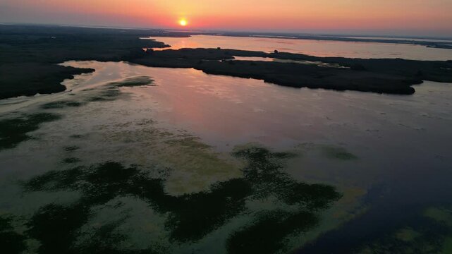 Spectacular high angle view of a golden sunrise over the Danube Delta UNESCO biosphere reserve. Scenic flyover above glowing water channels and wild reed vegetation in Romania.