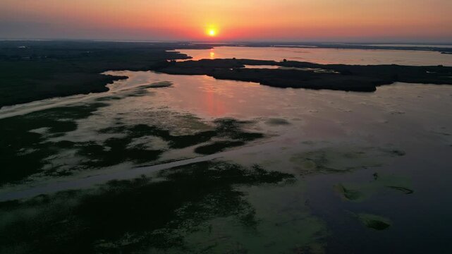 Spectacular high angle view of a golden sunrise over the Danube Delta UNESCO biosphere reserve. Scenic flyover above glowing water channels and wild reed vegetation in Romania.