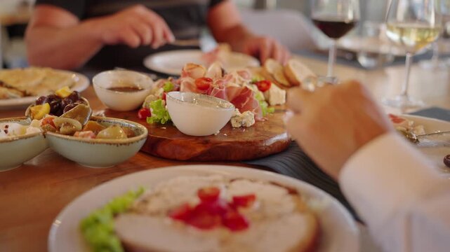 Close Up of People Eat Gourmet Food Table with Charcuterie Meat Board and Wine Glasses at Restaurant