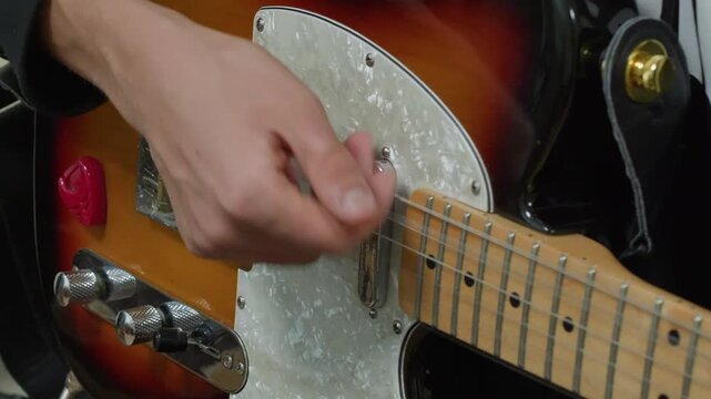 Close up of hands playing sunburst electric guitar with pearl pickguard, showcasing finger positioning on fretboard during performance.