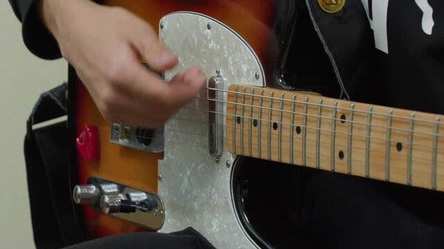 Close up of musician hands playing black electric guitar with white pearl pickguard, maple fretboard, capturing musical performance detail.