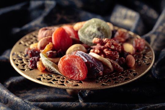 Dried tropical fruits and nuts in a golden bowl.