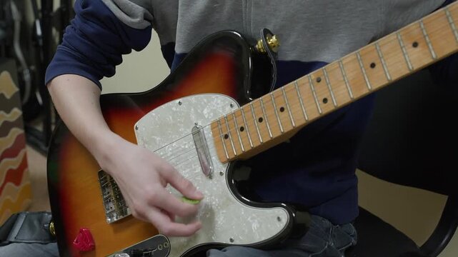 Close up of hands playing sunburst electric guitar with pearl pickguard, musician wearing blue sleeve detail while practicing music.