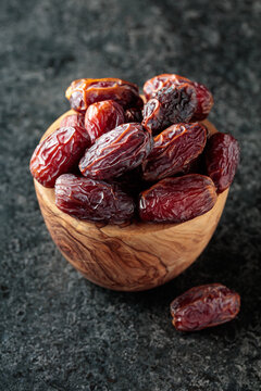 Dried dates fruit in wooden bowl on a black table.
