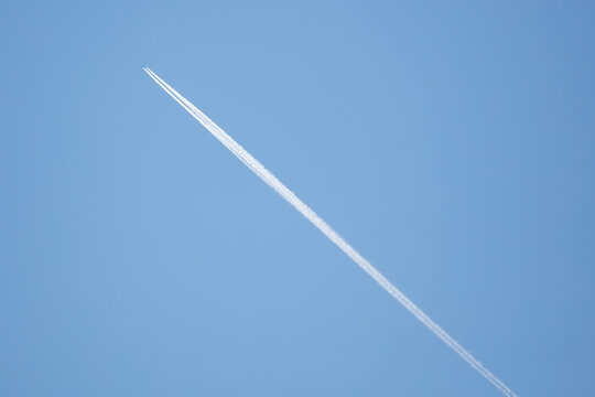 White vapor trail from airplane against bright blue background