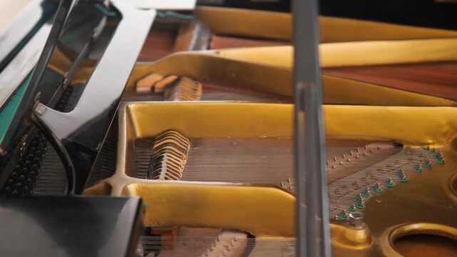 Wide shot of the internal mechanism of a grand piano with a golden frame and strings. Detailed footage of a classical musical instrument's action.