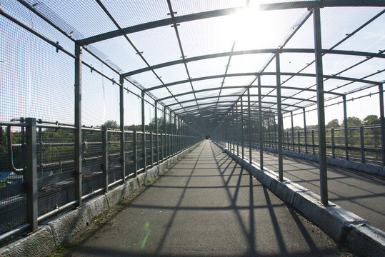 Symmetrical caged bridge footbridge with steel mesh security canopy over a pedestrian walkway.