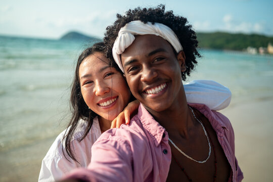 Diverse couple connected, embracing technology and social media while enjoying moments at the beach