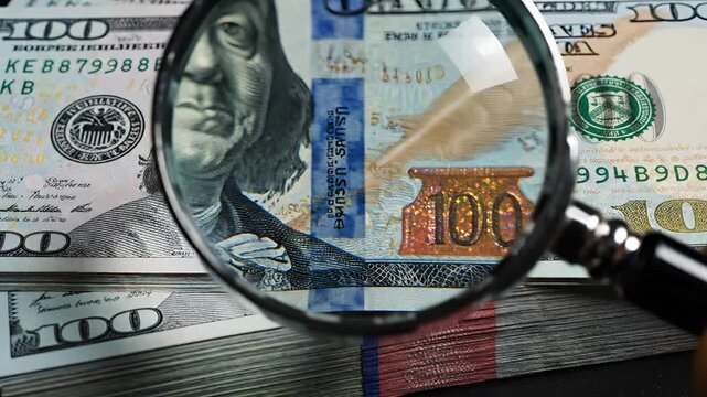 Magnifying Glass Examines Stack of US Hundred Dollar Bills Close Up.