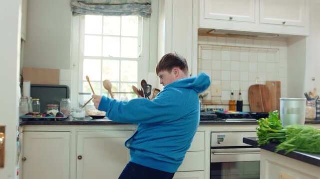 Kitchen, dance and teen with spoon, jump and performance for cooking success and moving with energy. Dancer, active and person with down syndrome, juggle and celebration for culinary skills in house