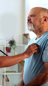 Indian Asian handsome male doctor attentively examines a senior old-aged male patient using a stethoscope in his OPD, focusing on accurate diagnosis and quality healthcare in a cozy clinic setting