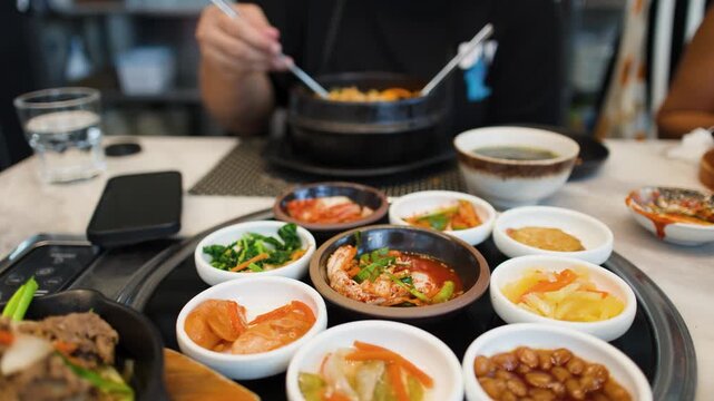 Person Eating Traditional Korean Banchan and Spicy Stew with Metal Chopsticks