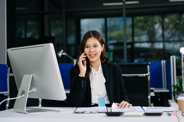 Fototapeta premium Professional Asian businesswoman talking on smartphone while working in modern office, corporate communication and productivity concept.