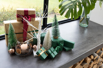 Naklejka premium Holiday display sitting on stone windowsill with wrapped kraft gifts, bottlebrush trees, lit candle
