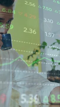 Vertical video: Man sipping coffee then reaching device in office, live market overlay showing data