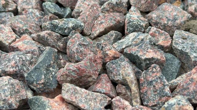 Close-up medium rubble gravel in daylight, dense spread of angular crushed stones with pink and gray tones, tight composition