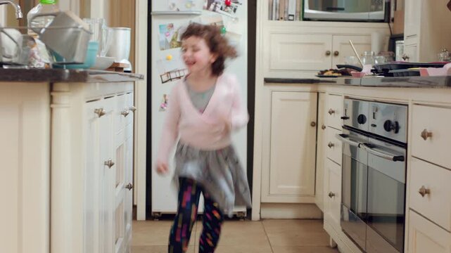 Face, child and energy with playing in home for development, restless movement or jumping. Active girl kid, person with adhd and hyperactivity in kitchen with running, dancing or impulsive on weekend