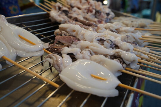 Close up full frame of fresh, clean white raw squids and cuttlefish on sticks ready for customers to order at a night market seafood stall.